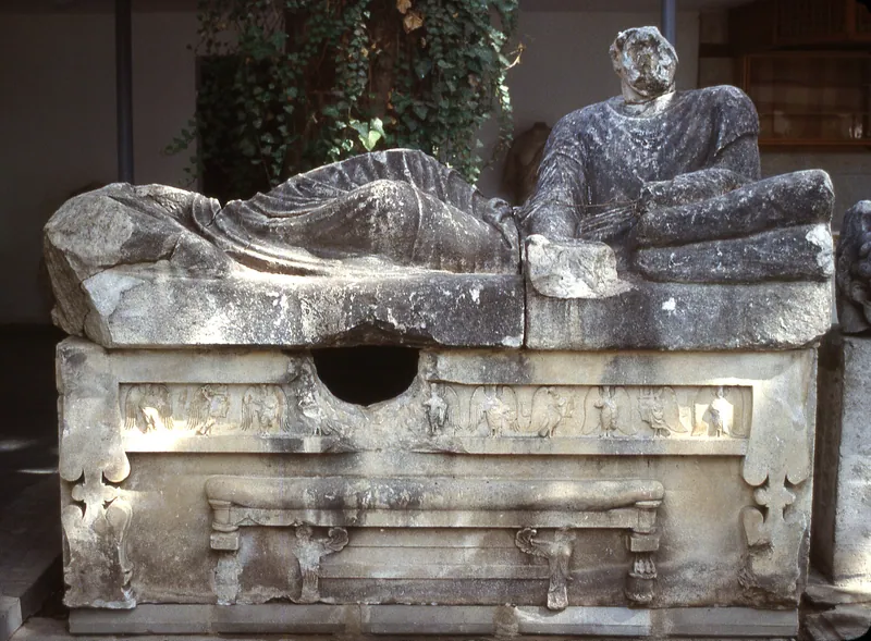 Sarcophagus on display in a museum: reclining figures on the lid, a frieze of winged figures on the front