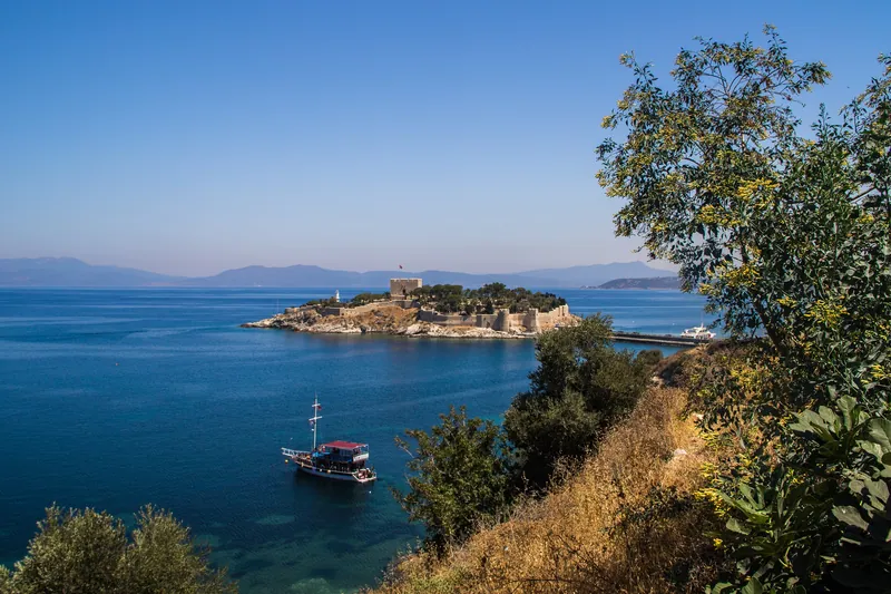 Kuşadası kıyısından körfez ve Güvercinada manzarası; denizde bir gezi teknesi